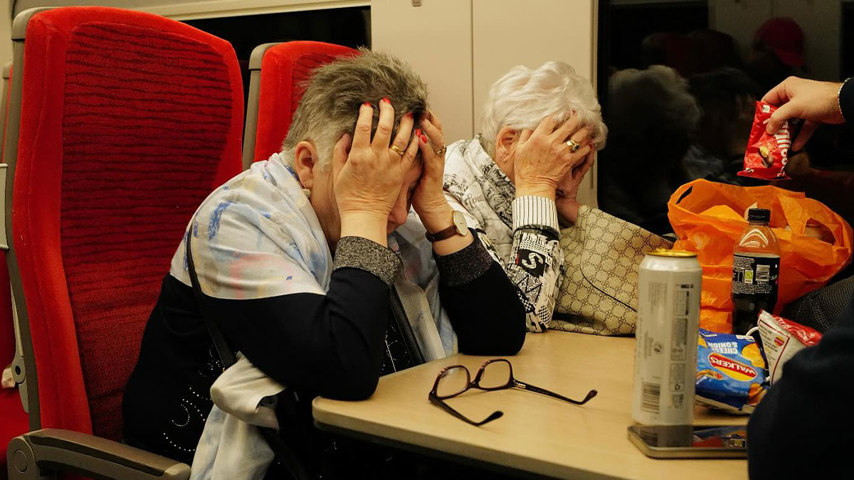 Two elderly women covering their faces with hands seated on a train in a perfectly timed street photo moment.
