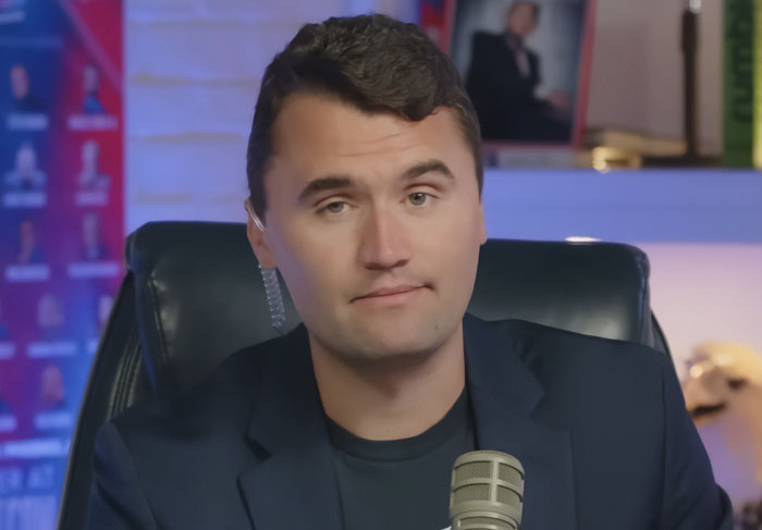 Charlie Kirk in a studio setting, wearing a dark blazer, speaking into a microphone with a serious expression. Charlie Kirk in a studio setting, wearing a dark blazer, speaking into a microphone with a serious expression.