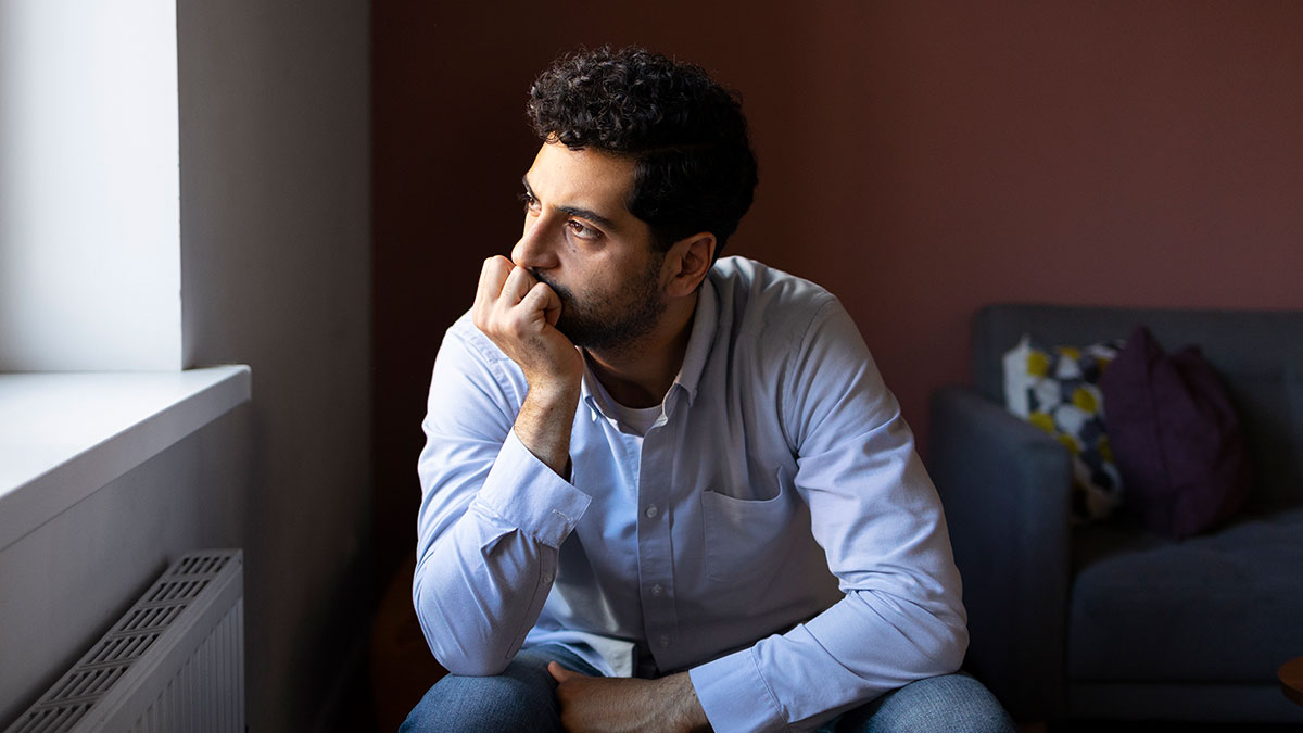 Pensive husband discovering cheating, planning pro revenge, sitting thoughtfully near a window in a dimly lit room.