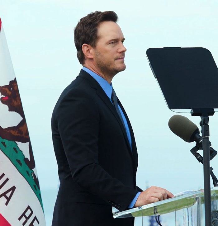 Chris Pratt speaking at a podium with a microphone and California flag, criticized for his unusual way of praying. Chris Pratt speaking at a podium with a microphone and California flag, criticized for his unusual way of praying.