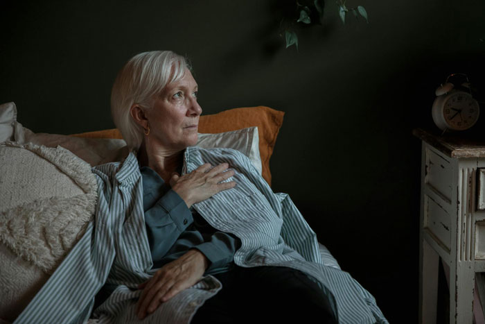 Older woman in striped pajamas sitting on bed with hand on chest, reflecting on Christian rapture and money concerns. Older woman in striped pajamas sitting on bed with hand on chest, reflecting on Christian rapture and money concerns.