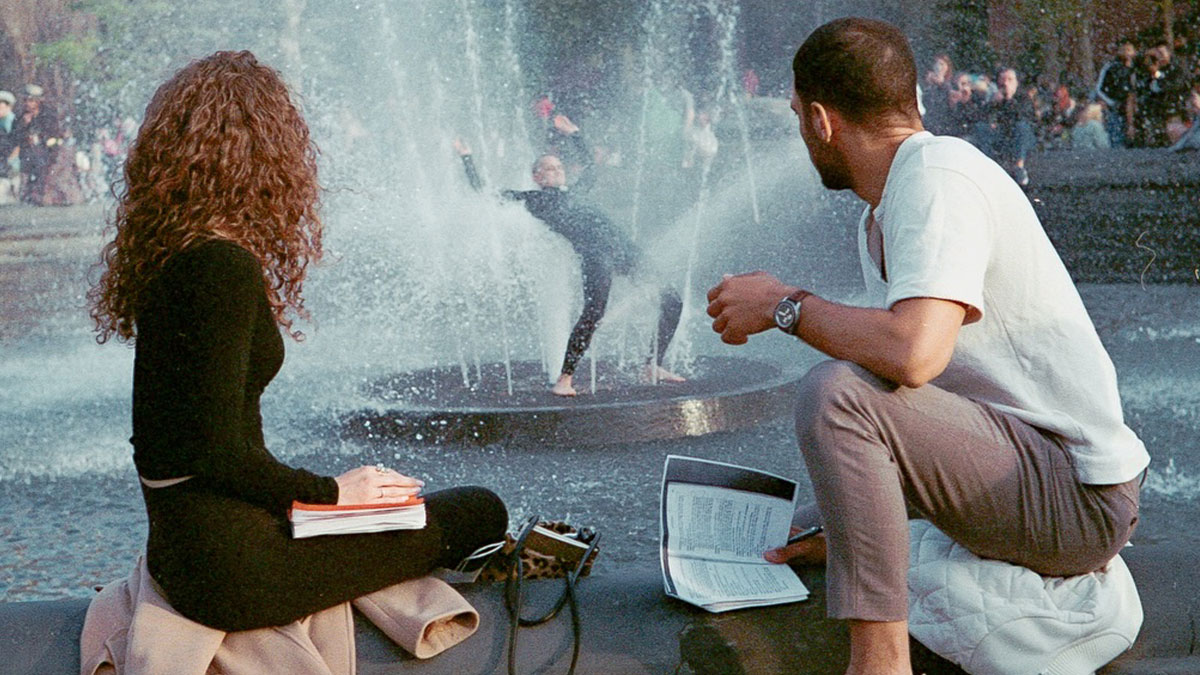 Two people observing a street performer dancing in a fountain, capturing striking street photos like movie stills.