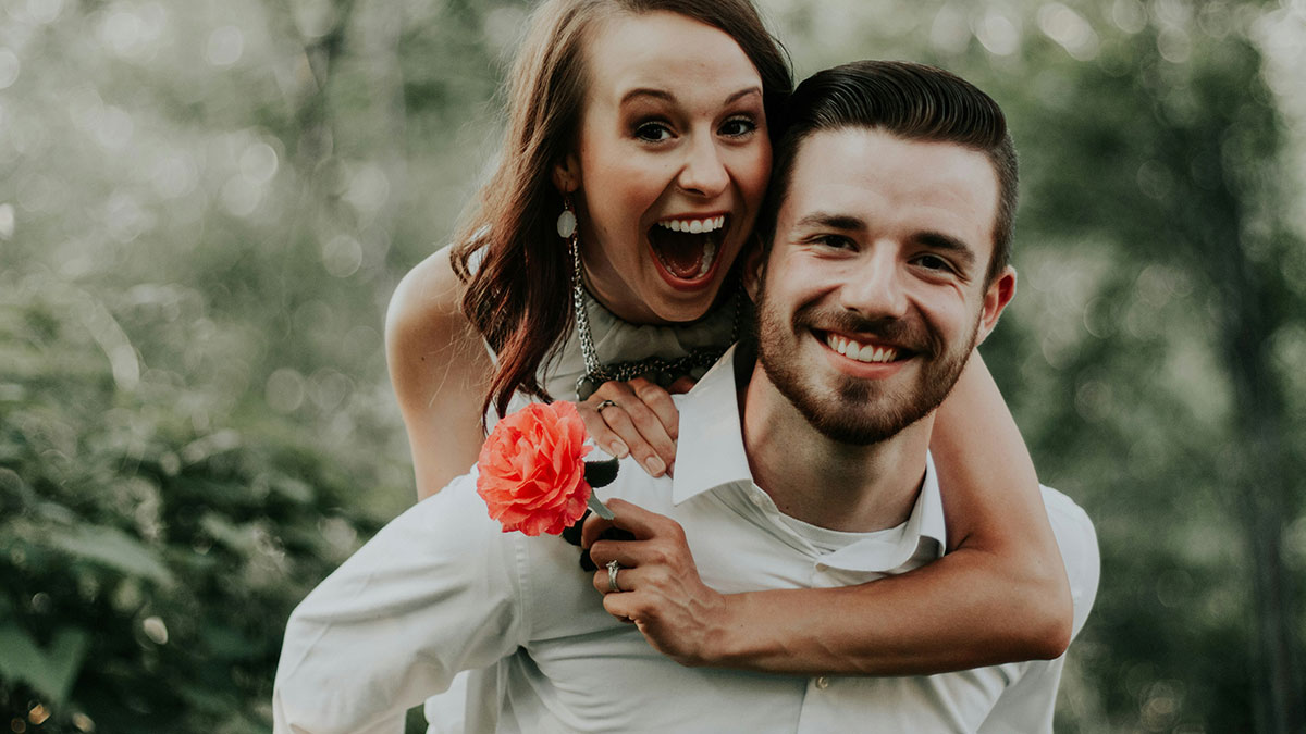 Happy couple outdoors sharing a joyful moment with a bright flower, representing wholesome relationship memes and love.