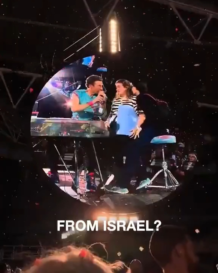 Chris Martin on stage interacting with fans during a concert, amid political speech backlash and controversy. Chris Martin on stage interacting with fans during a concert, amid political speech backlash and controversy.