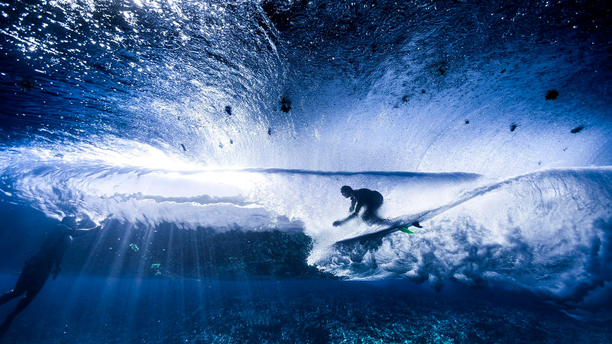 Surfer riding a wave underwater with light beams revealing earthu2019s hidden patterns in stunning vibrant colors.