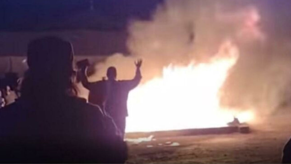 Person with raised hands near large fire and thick smoke at night, illustrating actions meet consequences in a chaotic scene.
