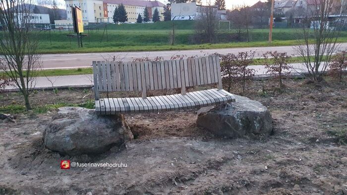 Unstable construction design showing a wooden bench balanced awkwardly on two large rocks in an outdoor setting.