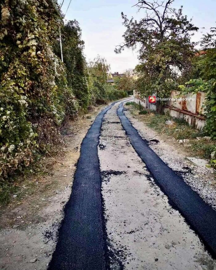 Poorly executed construction showing two narrow asphalt strips on an unfinished and damaged road surface.