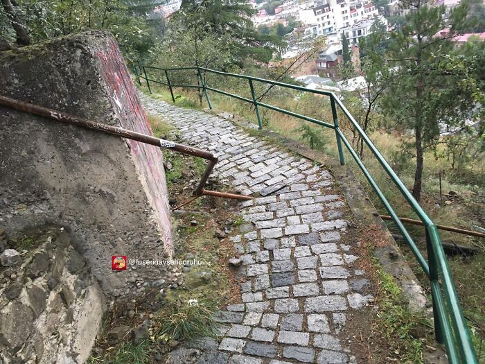 Uneven stone path with a poorly placed bent metal railing, an example of strange construction and design flaws.
