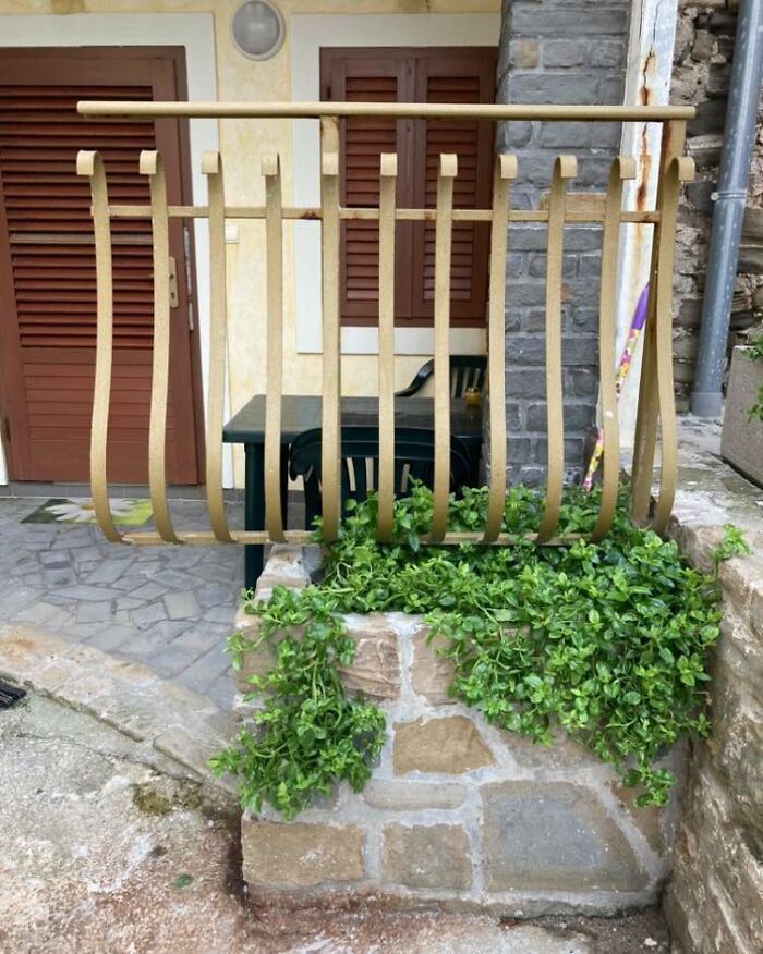 Construction fail showing a warped metal railing installed above a small stone planter with greenery.
