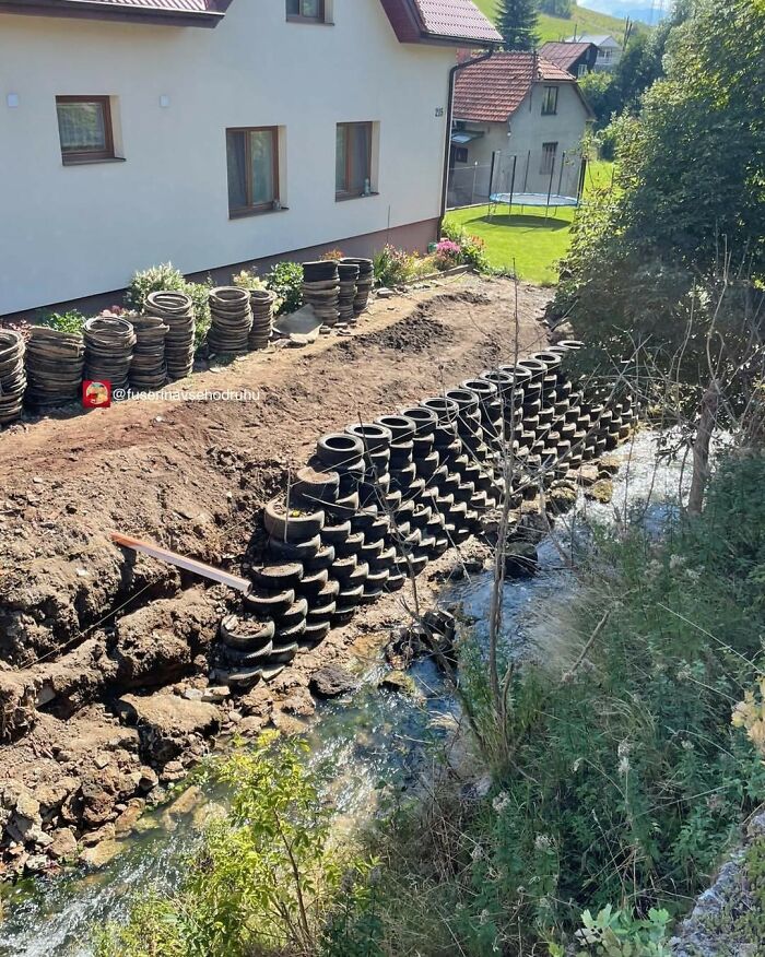 Retaining wall made of stacked tires alongside a small stream next to a house and garden area under construction.