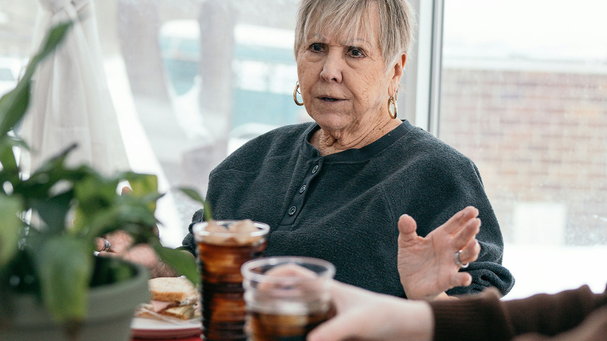 Older woman speaking seriously at a table with drinks, representing MIL poisoning toddler with essential oils incident