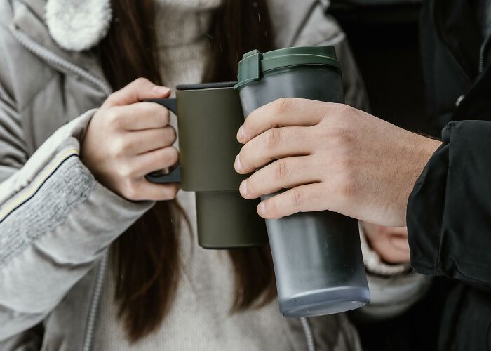 Two people holding reusable travel mugs, illustrating overhyped products many say to stop buying.