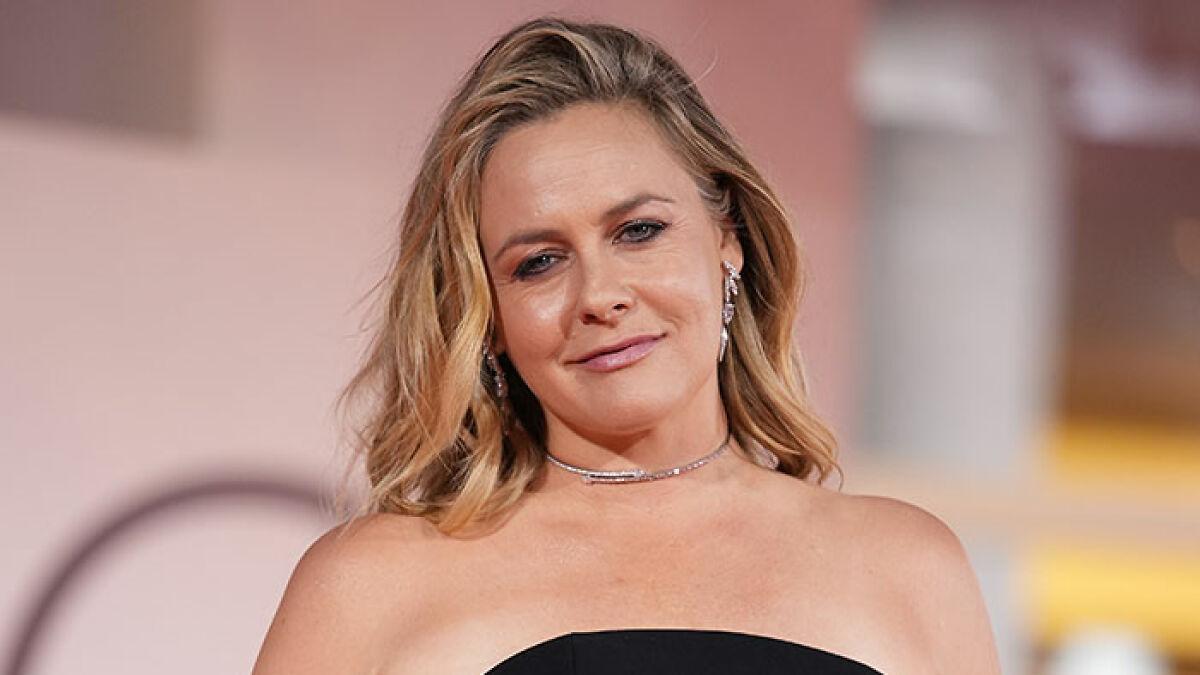 Alicia Silverstone wearing elegant earrings and a choker, smiling and turning heads at a Venice event.