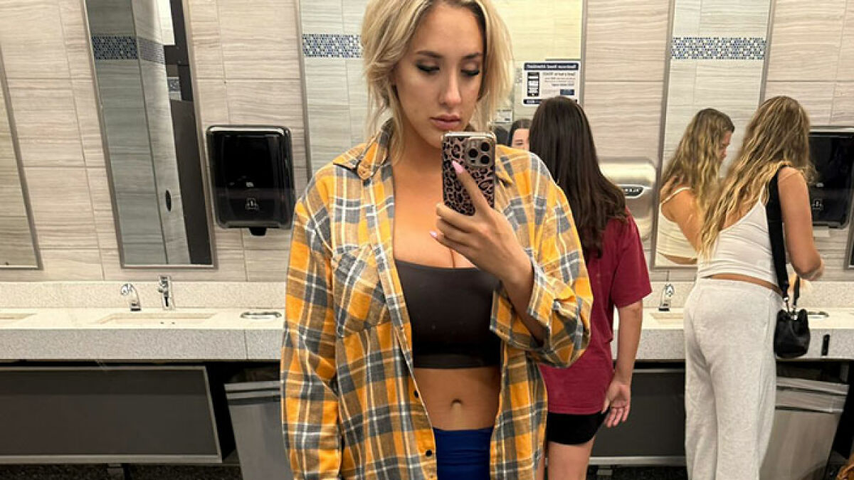 Model taking a mirror selfie in a yellow plaid shirt and black top, relating to big breasts discrimination on a flight.