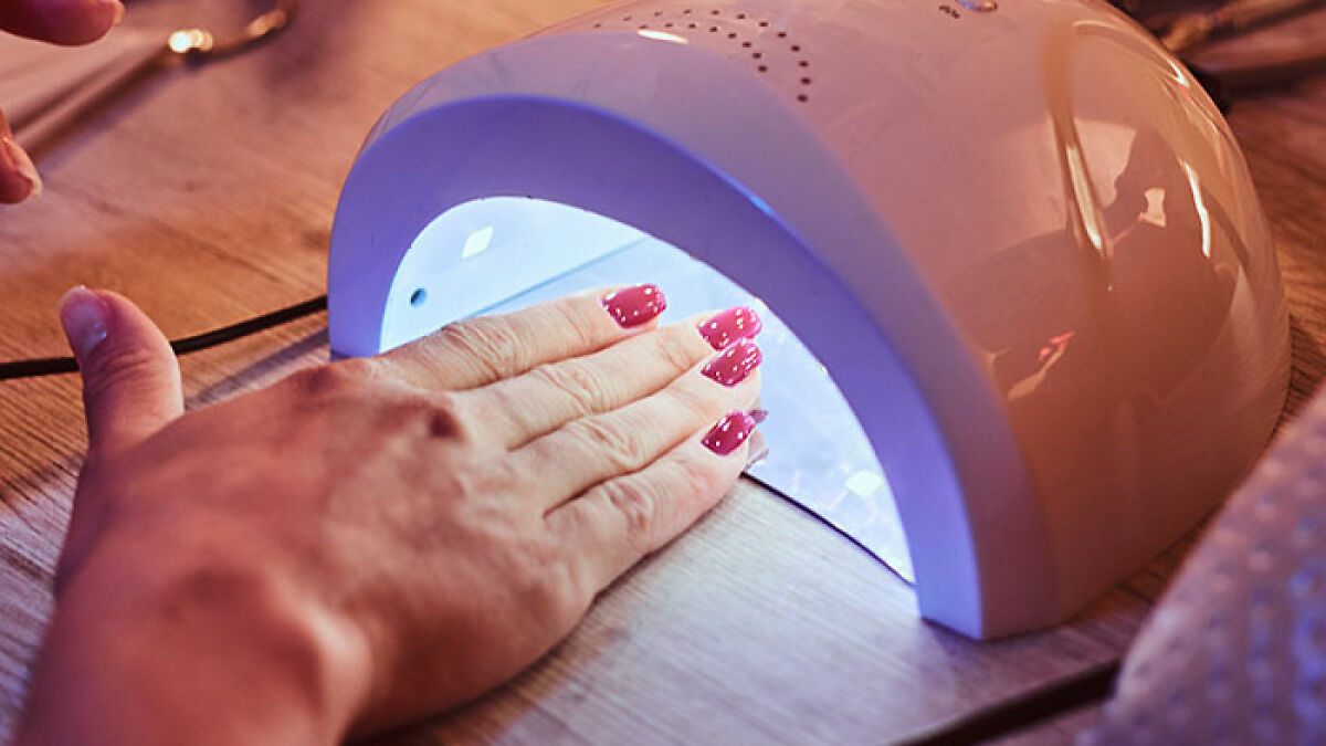 Hand with gel nail polish drying under a UV lamp, illustrating gel nail polish use and regulations in different regions.