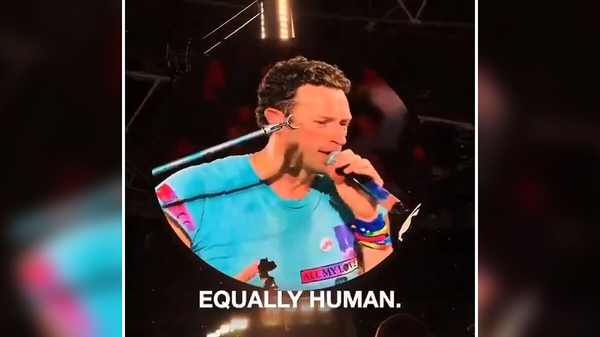 Chris Martin performing on stage wearing a blue shirt with microphone in hand during a viral concert moment.