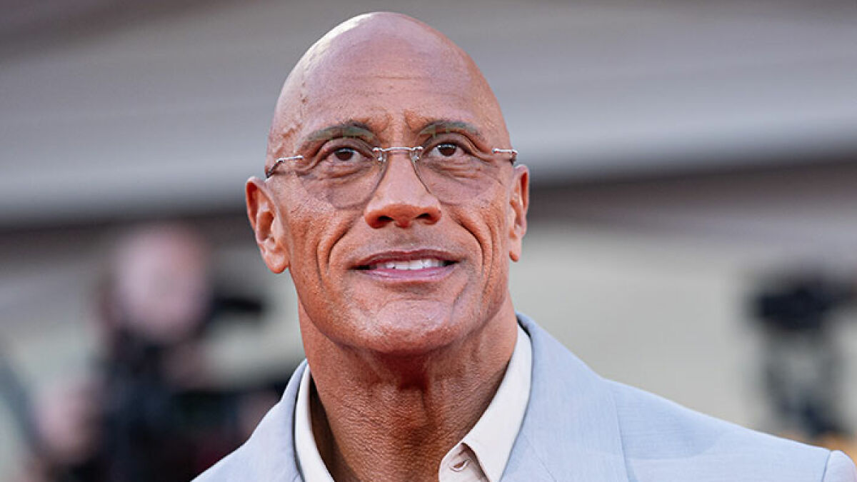Dwayne Johnson wearing glasses and a light suit jacket at an outdoor event, showing his new slim look.
