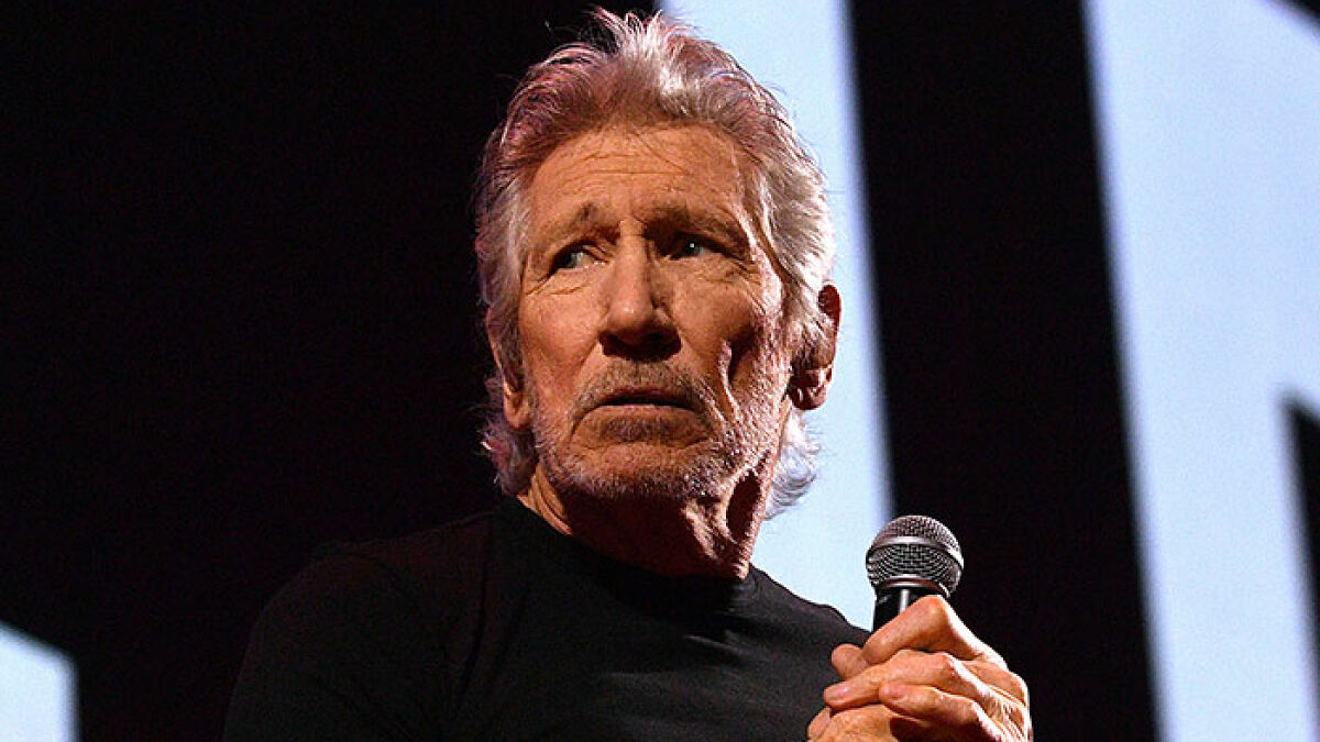 Roger Waters on stage holding a microphone, expressing serious emotion during a live performance.