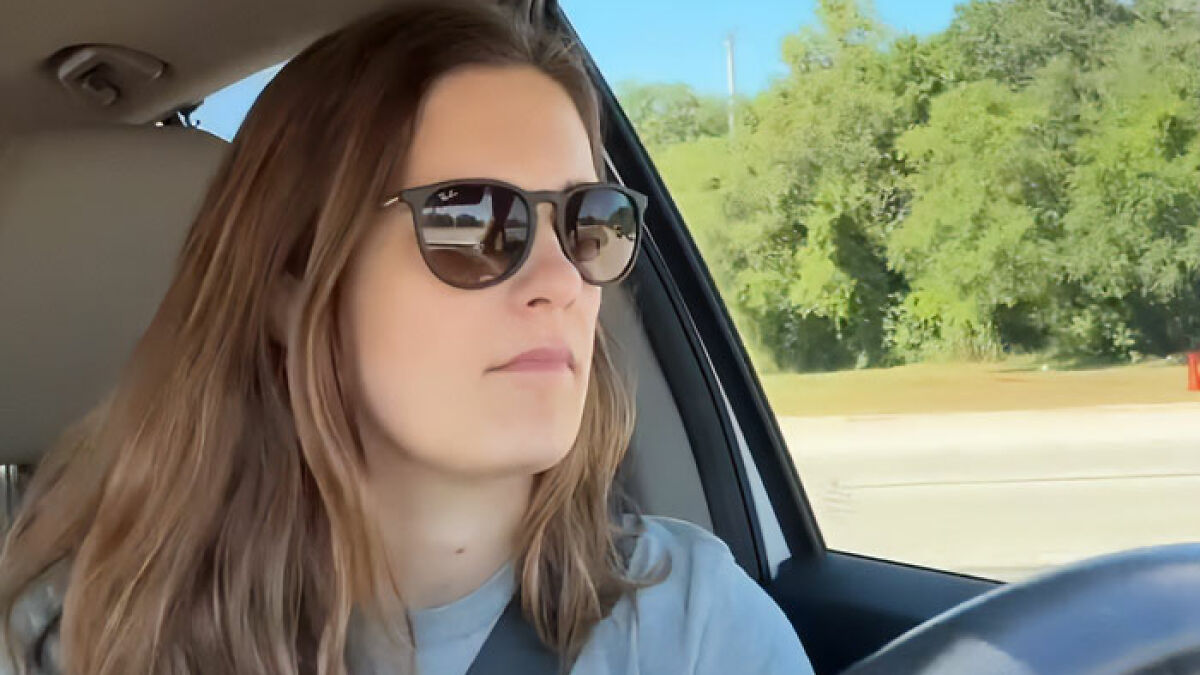 Woman driving a car wearing sunglasses, captured during a moment reflecting on mom telling daughter about Taylor Swift's wedding.