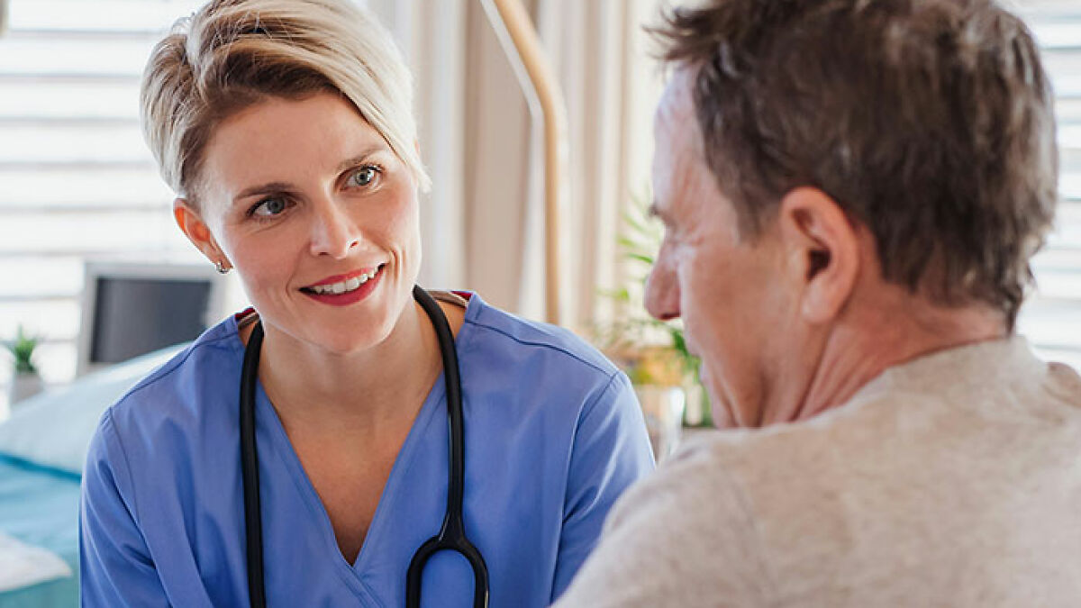 Female urgent care nurse in blue scrubs talking to a male patient in an exam room during a medical consultation