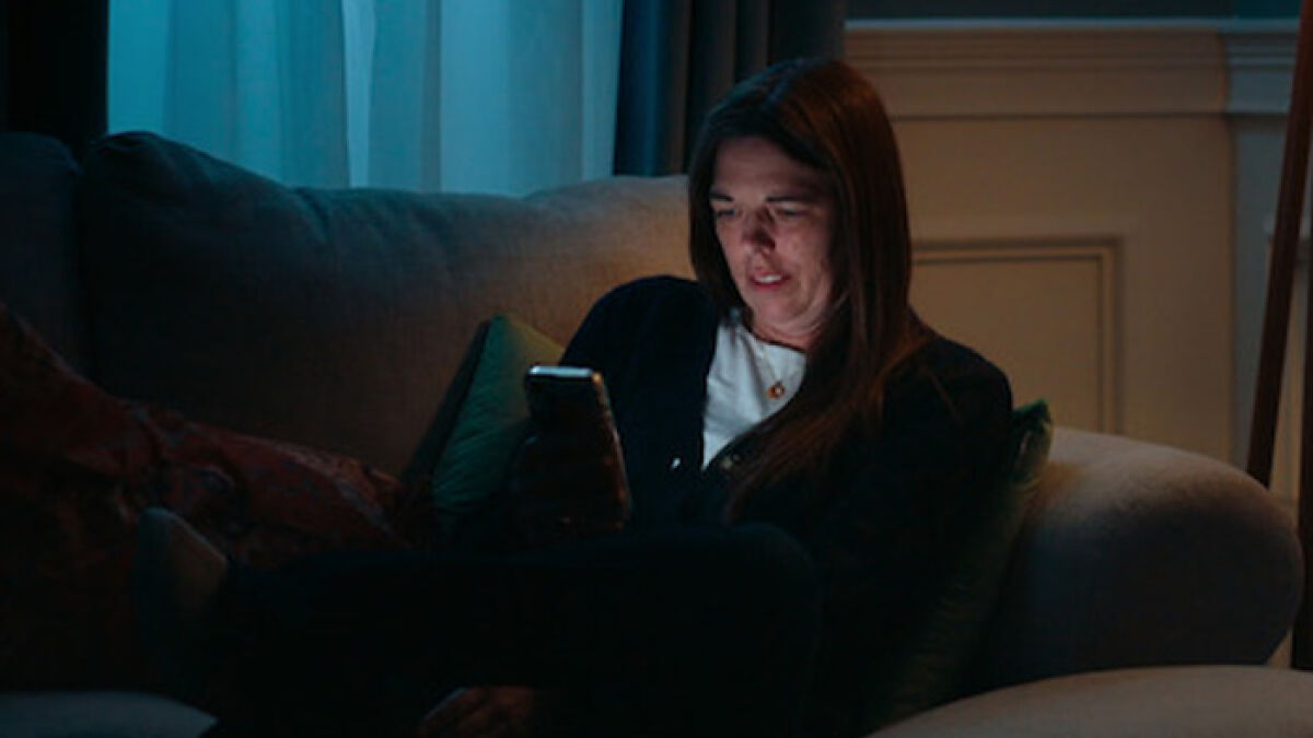 Woman alone on couch at night looking at phone screen, illustrating mom who catfished her daughter using Lo nickname threats