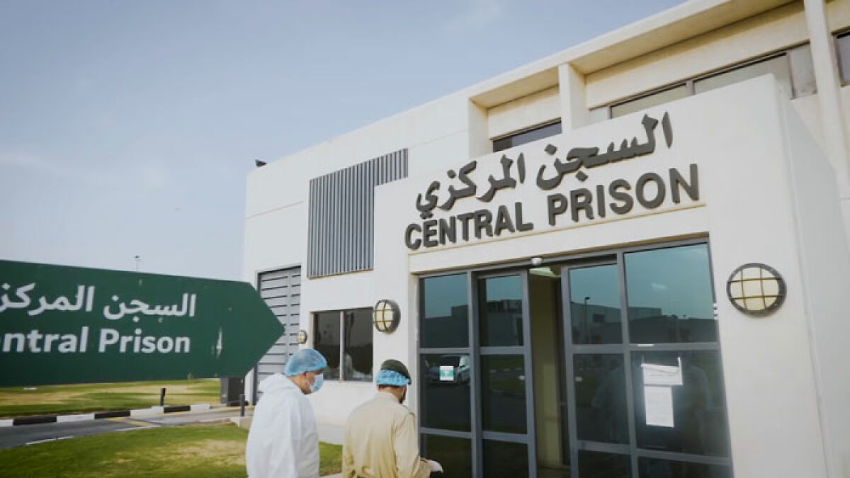 Exterior view of infamous Dubai central prison with two people walking towards entrance wearing protective head covers and masks.