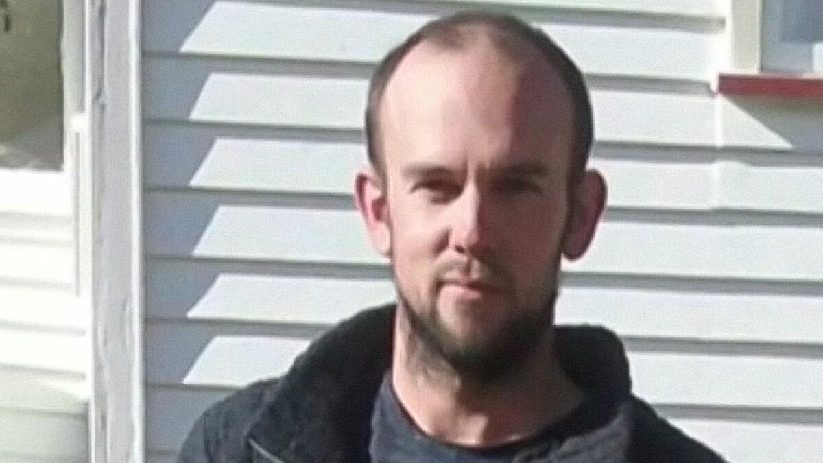 Man with beard and receding hairline standing outdoors near white siding, related to fugitive dad police standoff news.