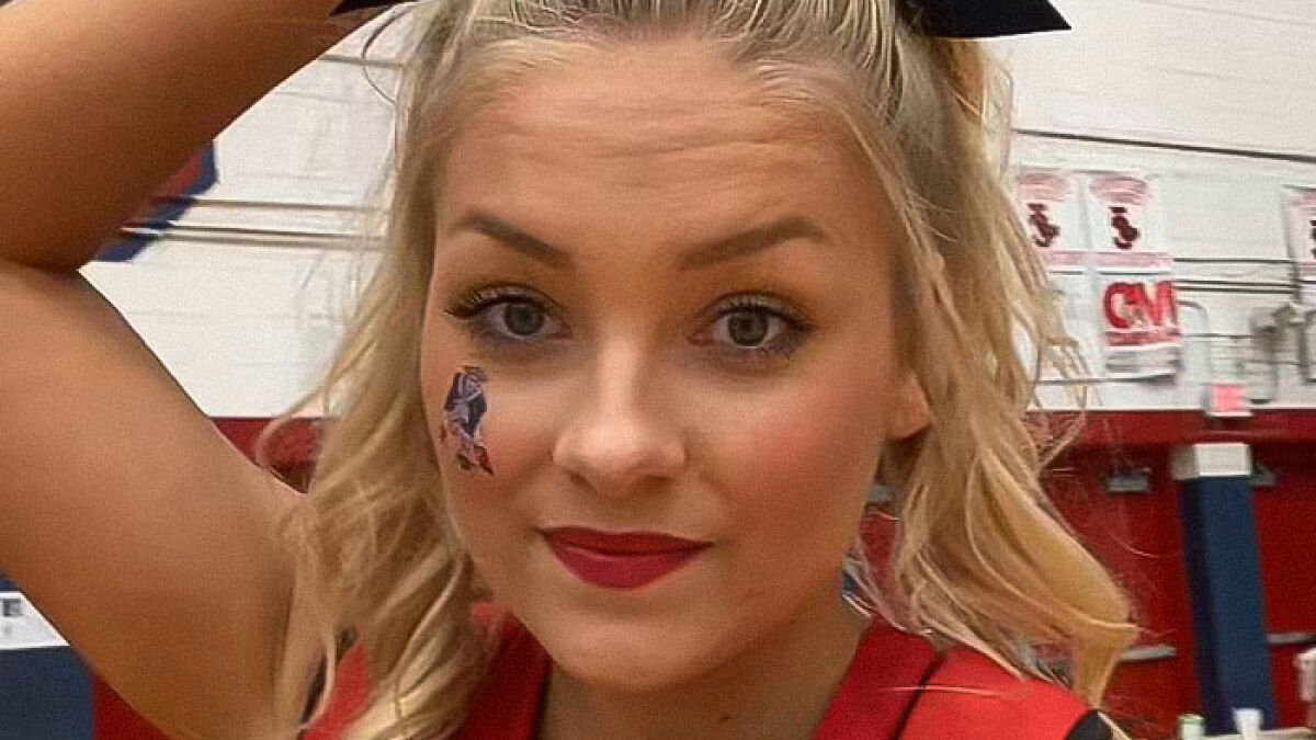 Cheerleader in uniform with face paint, posing indoors in a gym, related to news about newborn found in closet and university dropout.