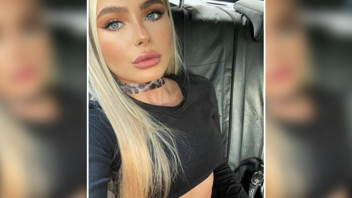 Young glamorous law student with long blonde hair in black top inside a car, facing camera with serious expression.