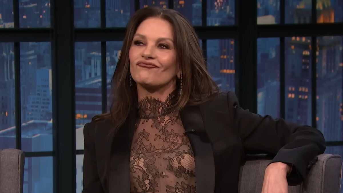 Catherine Zeta-Jones on a talk show, wearing a lace top and blazer, reacting to a comment about a young fan.