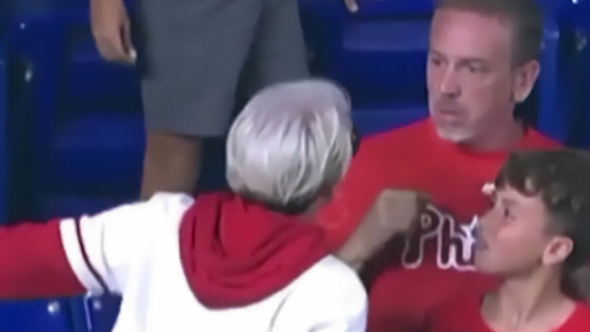 Dad in red Phillies shirt confronting woman with white hair during viral MLB ball incident at the stadium.