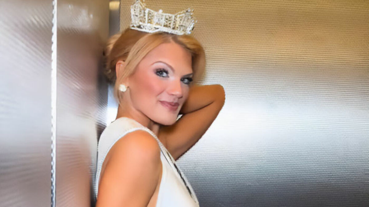 Miss America wearing crown and white dress, posing confidently against a metallic background after winning the pageant.