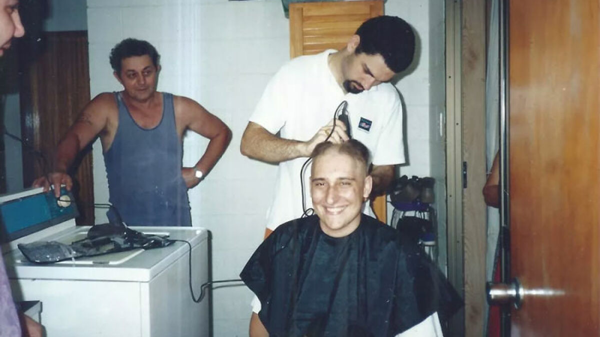 Man diagnosed with testicular cancer getting head shaved, smiling while a friend cuts his hair indoors