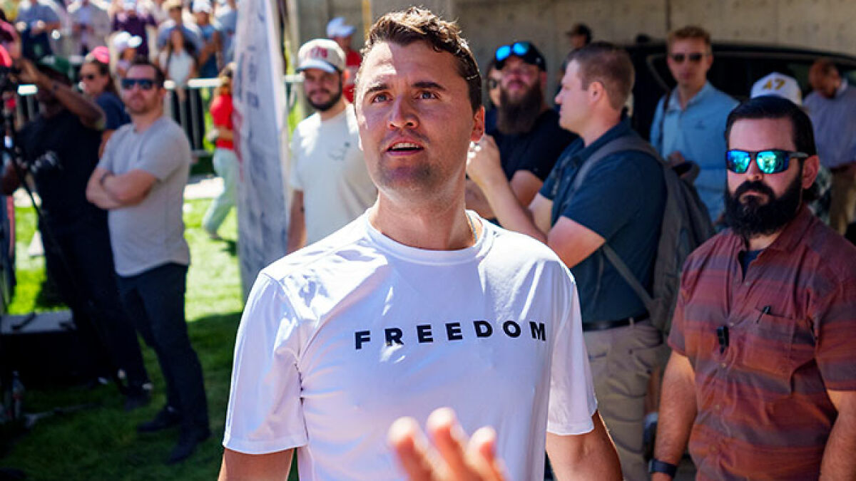 Man wearing white freedom shirt at outdoor event with crowd in background, related to Iryna Zarutska and Charlie Kirk crime case.