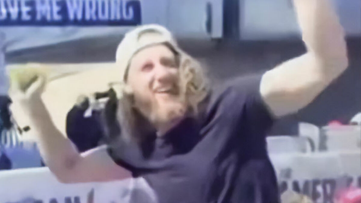 Bearded man in crowd cheering and looking back during Charlie Kirk's attack with a backward white cap and black shirt.