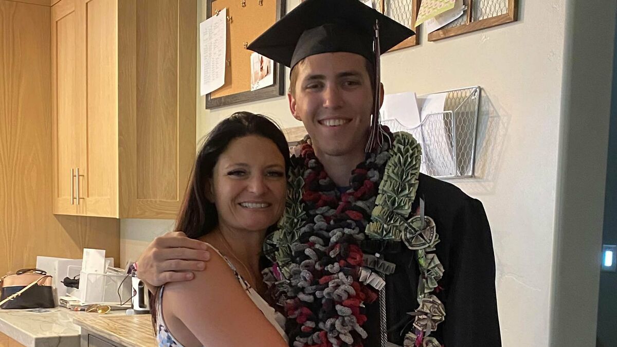 Young man in graduation cap and gown with floral leis hugging a woman in a kitchen setting, related to Charlie Kirk suspect news.
