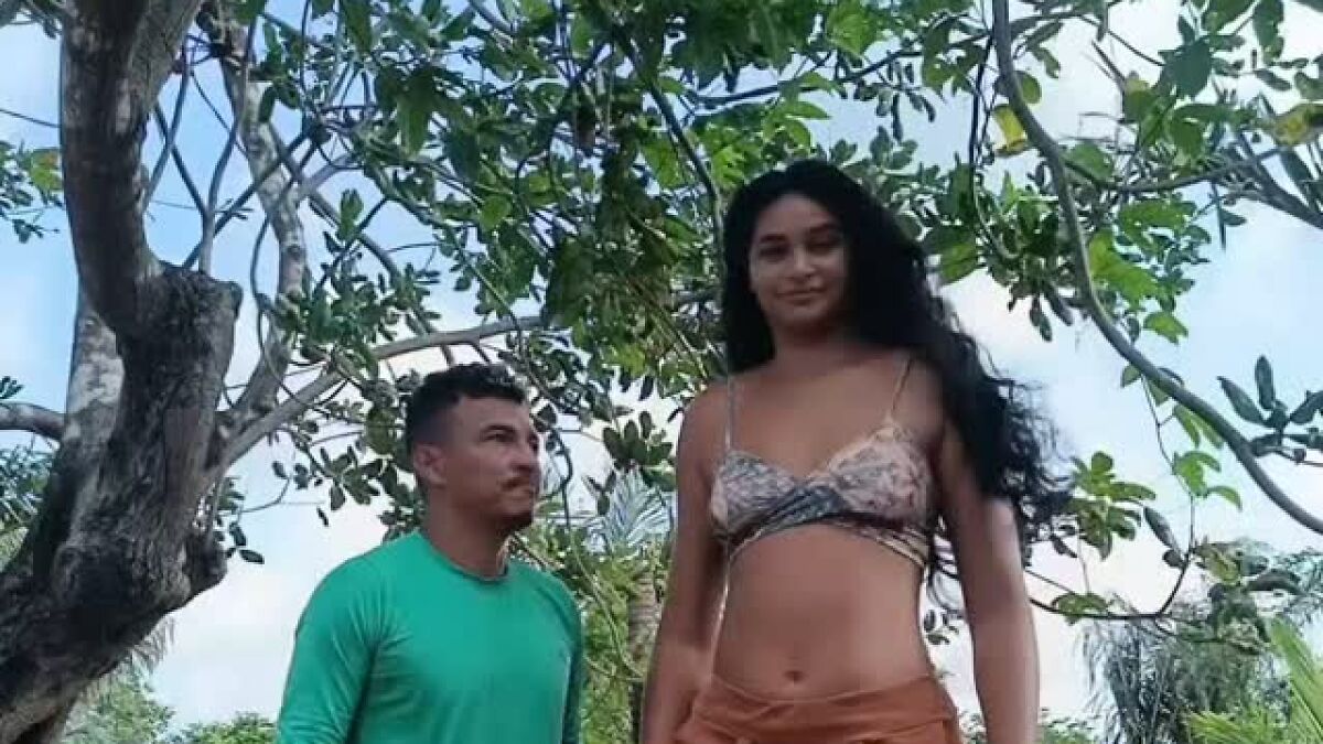 Tall woman 6u20199u201d standing next to her shorter 5u20194u201d husband outdoors with trees in the background.