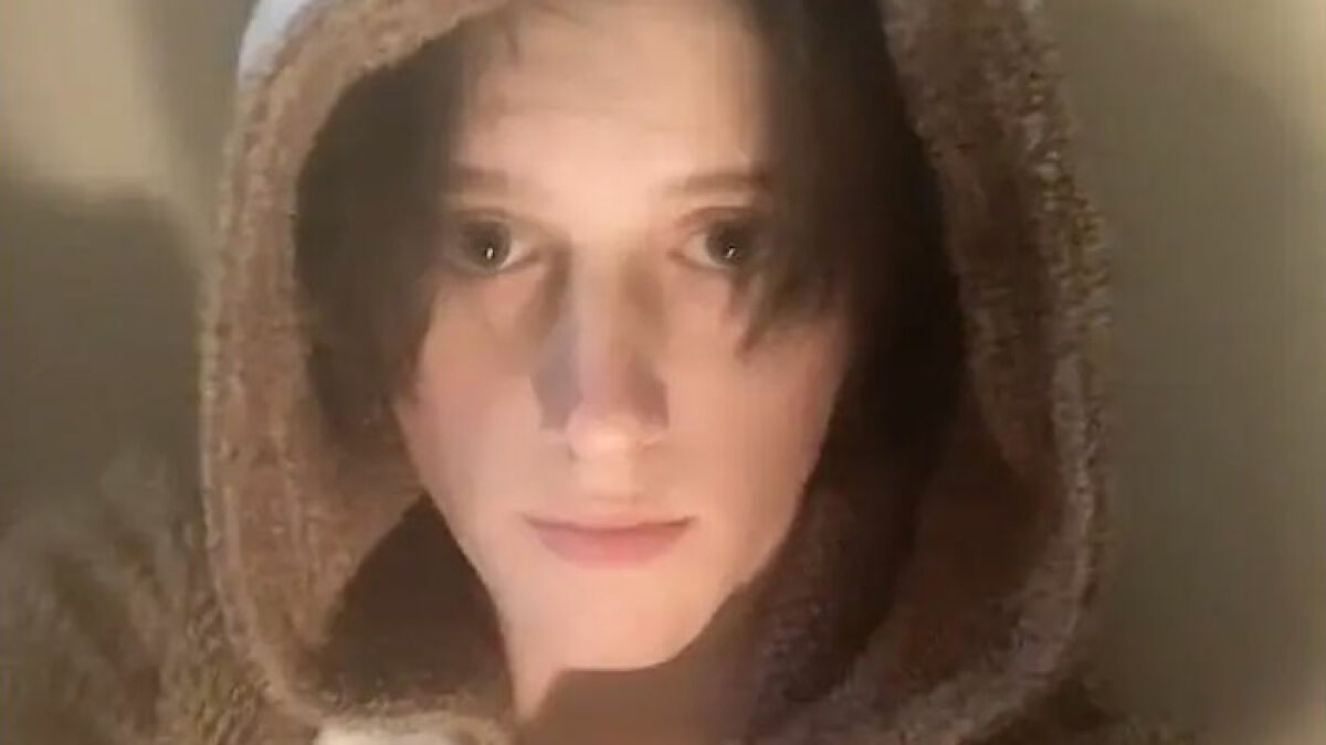 Tyler Robinson in a close-up photo wearing a brown hooded garment with a neutral expression visible.