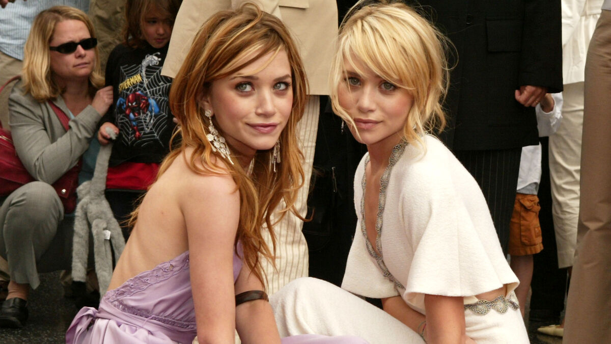 Mary-Kate and Ashley Olsen sitting side by side wearing elegant dresses, stunning fans with unrecognizable looks at NYFW.