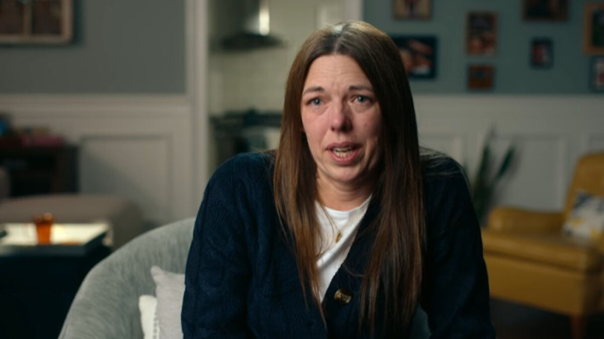 Woman with long brown hair sitting in a living room, making a shocking confession about anonymously bullying her daughter.
