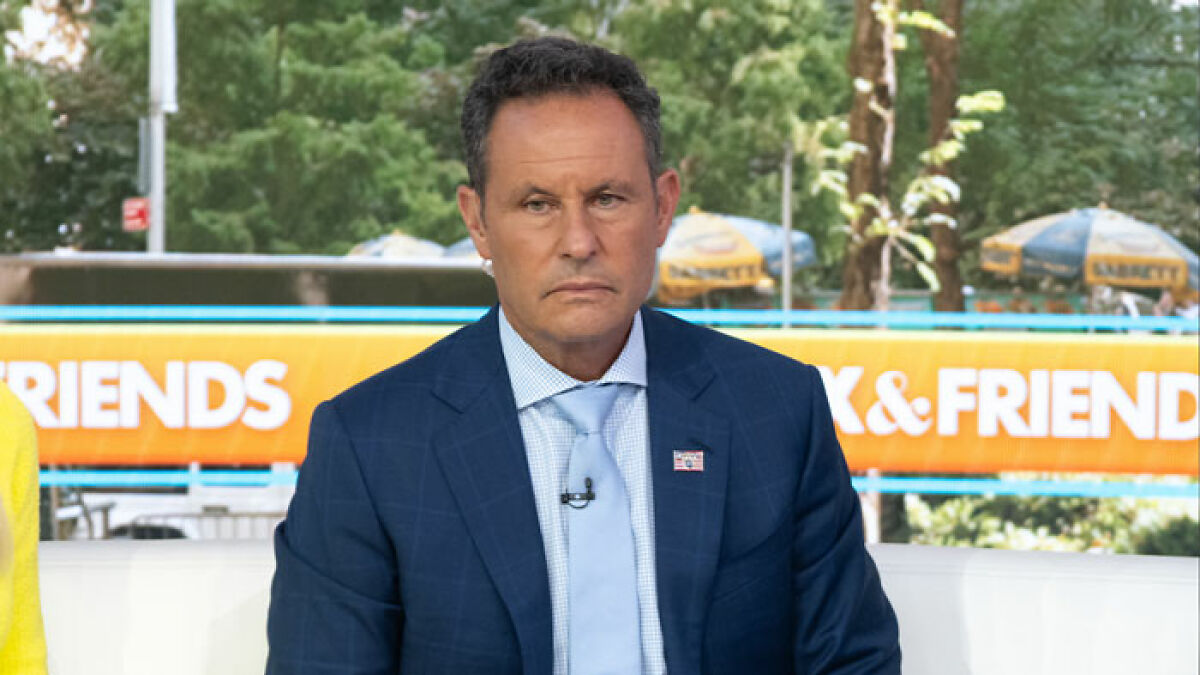 News host in a blue suit looking serious during a live discussion on Ukrainian refugee attack on outdoor TV set.