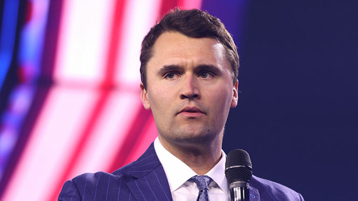 Man speaking into microphone at event with colorful background, related to falsely confessing to Charlie Kirk's assassin claim.