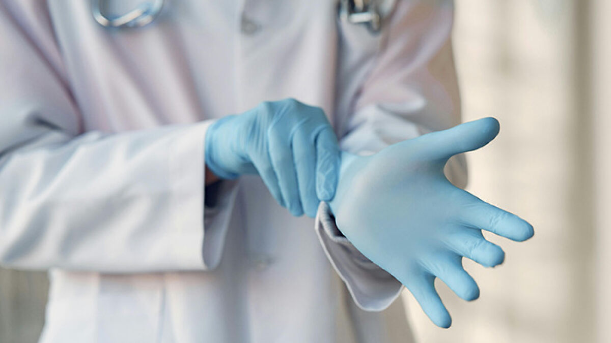 Doctor wearing blue surgical gloves preparing for surgery in a medical setting, emphasizing hospital care and procedure.