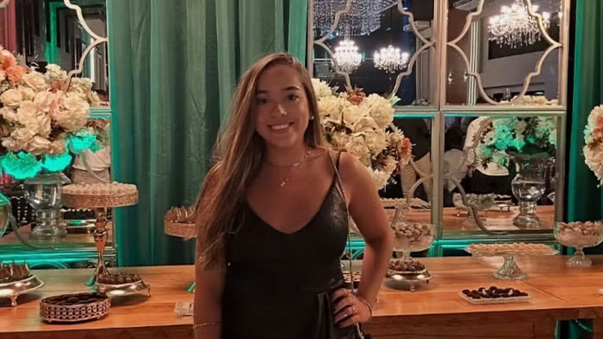 Young woman standing in front of floral decorations and mirrors, related to plastic surgeon arrest after b**t lift procedure gone wrong