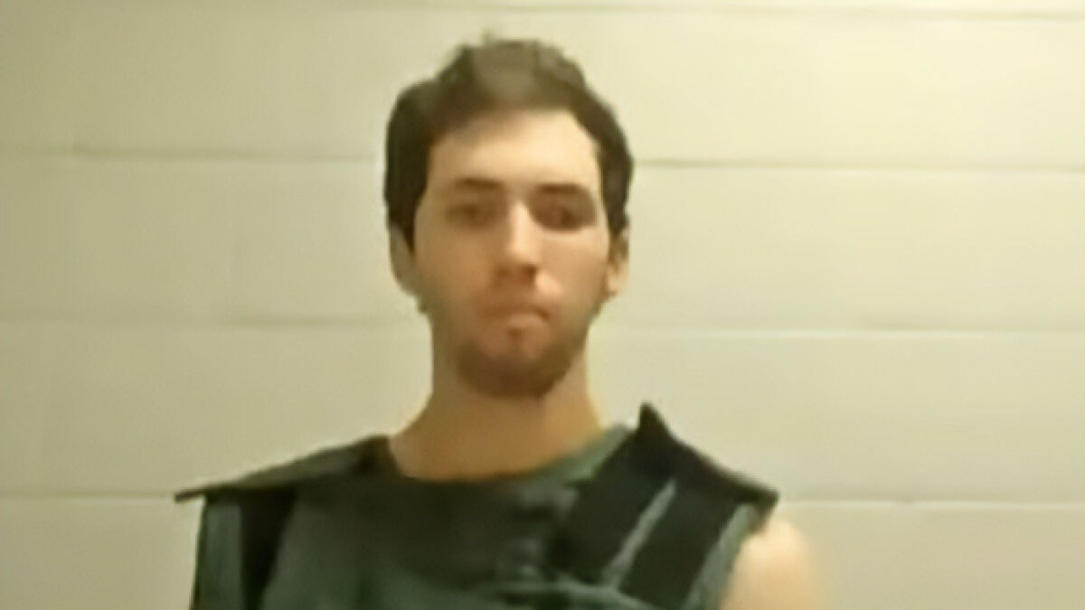Tyler Robinson appearing in court wearing a dark vest against a pale tiled wall in a low-resolution image.