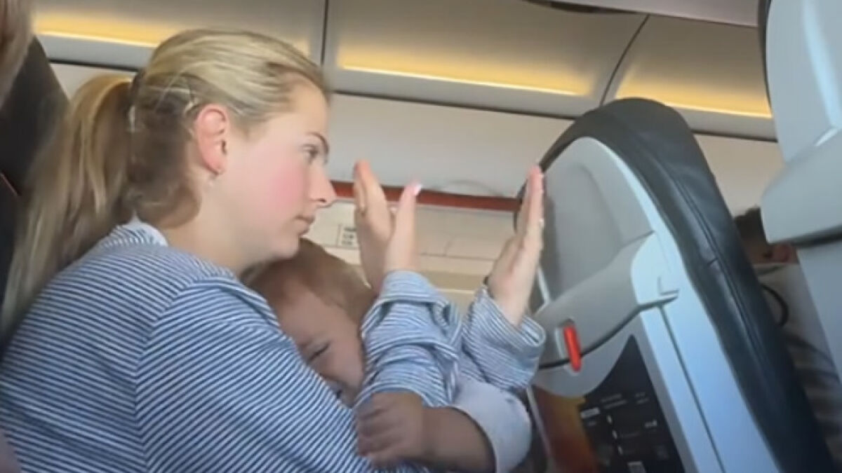 Annoyed mom with child reacting to reclined plane seat pressing against her on a crowded flight interior.