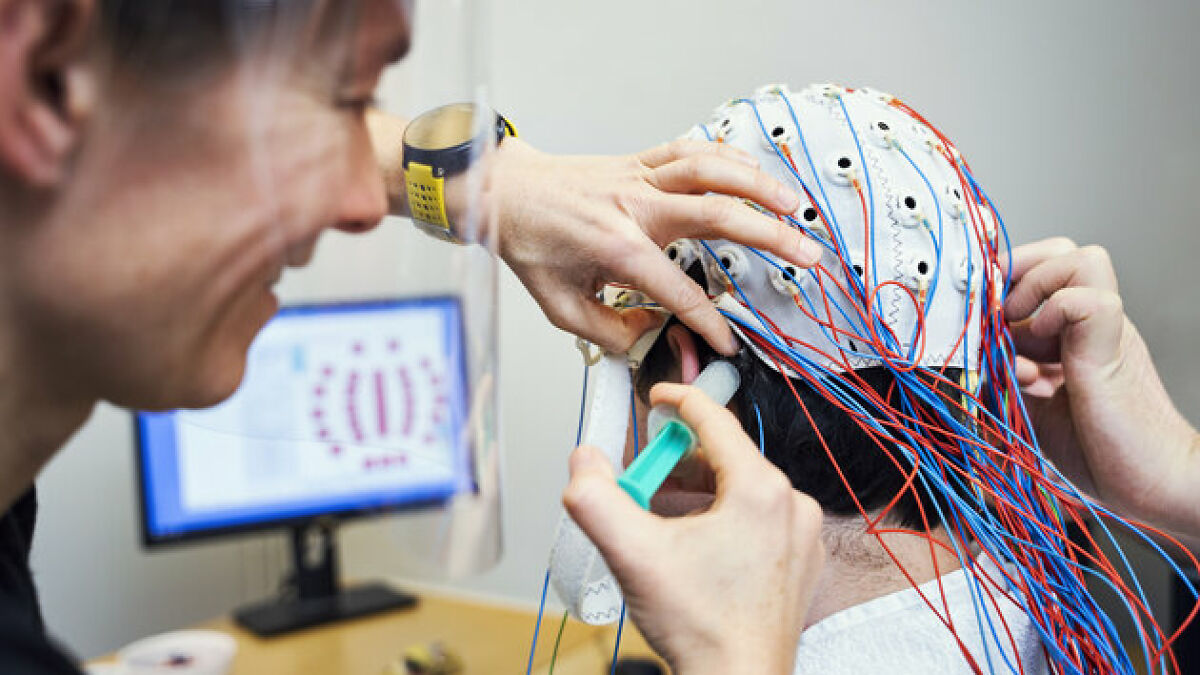 Scientist fitting EEG cap with many wires on personu2019s head to study brain activity related to gut feeling and precognition.