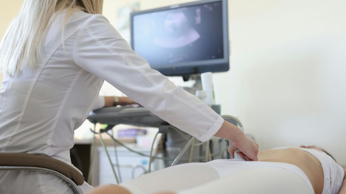 Female doctor performing ultrasound scan on a young womanu2019s abdomen during unexpected diagnosis of period absence.