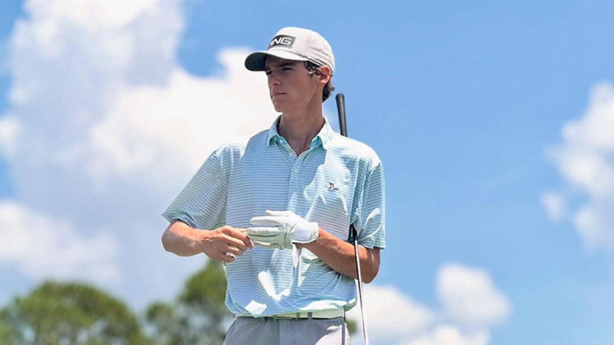Teen golfer practicing on a sunny course wearing a light blue shirt and white cap with a golf club.